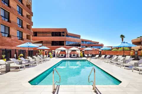 Resort pool deck with turquoise water, lounge chairs, blue umbrellas, and brick building