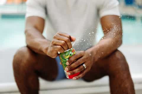 Person in white shirt holding colorful drink with water splashing at beach
