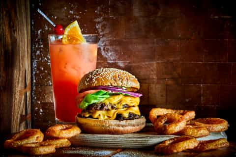 Gourmet burger with double cheese and crispy onion rings served with a red cocktail