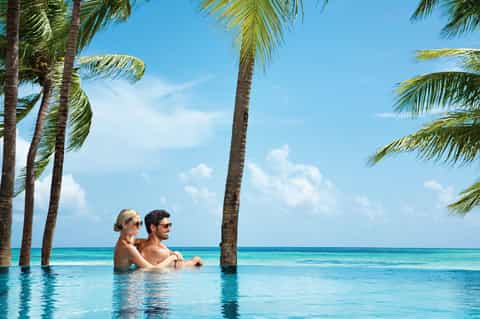 Couple relaxing in infinity pool with palm trees and ocean view at tropical resort