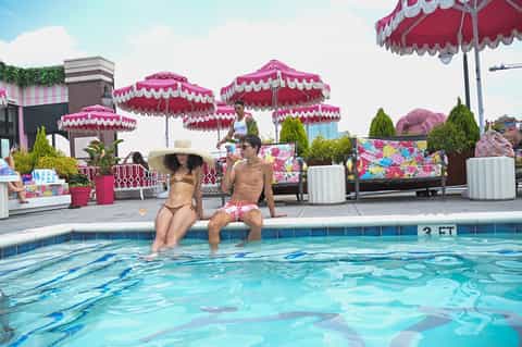 Rooftop pool with pink umbrellas and two guests sitting at the edge on a sunny day