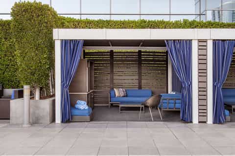 Modern poolside cabana with blue sofa, chairs, and striped curtains surrounded by hedges