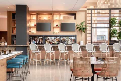 Modern hotel bar and lounge with wooden shelving, white bar stools, and terracotta seating areas