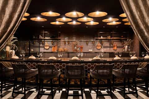 Upscale bar with black bar stools, warm pendant lighting, and bronze-trimmed countertop