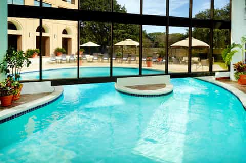 Indoor pool with spa feature, large windows overlooking outdoor pool and landscaped grounds