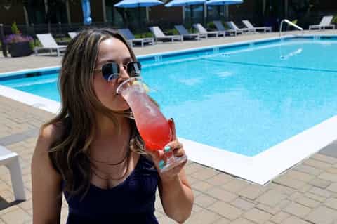 Woman in sunglasses drinking a pink cocktail by a resort swimming pool