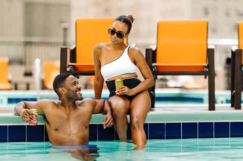 Couple enjoying beverages by indoor pool with yellow lounge chairs in background