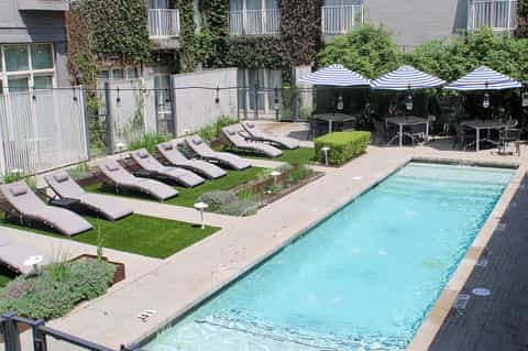 Resort pool deck with loungers, blue striped umbrellas, dining area, and ivy-covered building facade