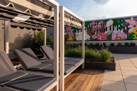 Modern rooftop terrace with lounge chairs under striped umbrellas and colorful floral mural artwork