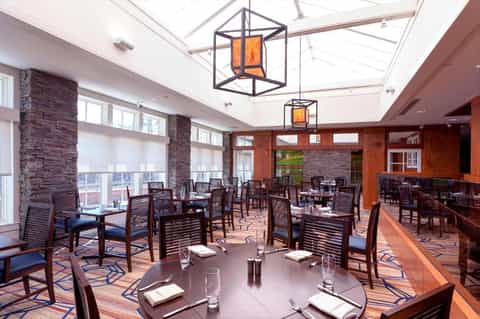 Modern restaurant dining room with stone pillars, skylights, geometric pendant lights, and window views