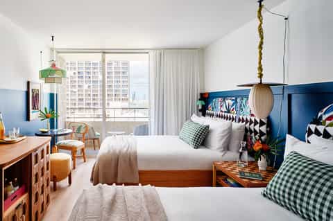 Modern hotel room with two beds, blue headboard, city view balcony, and contemporary decor with green and white accents