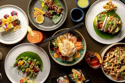 Overhead view of colorful Asian fusion dishes with noodles, vegetables, and sauces on multiple plates