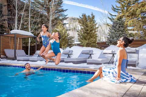 Family enjoying heated outdoor pool with snowy landscape and evergreen trees in winter mountain setting