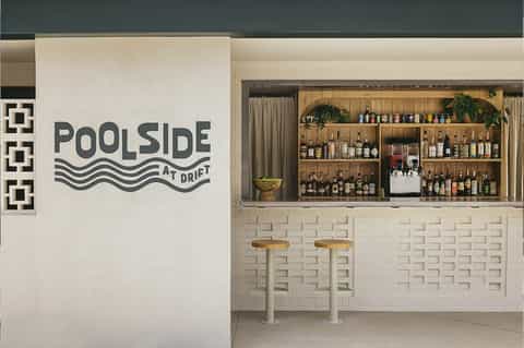 Poolside bar interior at Drift with white subway tile, wooden shelving, and striped bar stools