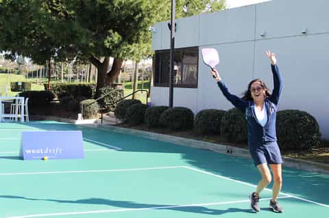 Woman playing pickleball on bright turquoise court at resort