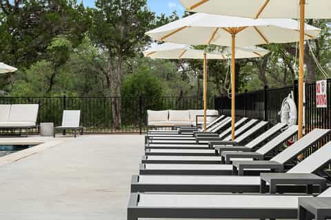 Resort pool deck with lounge chairs and cream umbrellas overlooking forested landscape