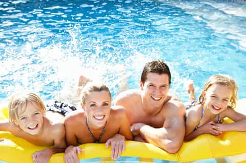 Family of four enjoying a yellow pool raft in a sparkling blue swimming pool