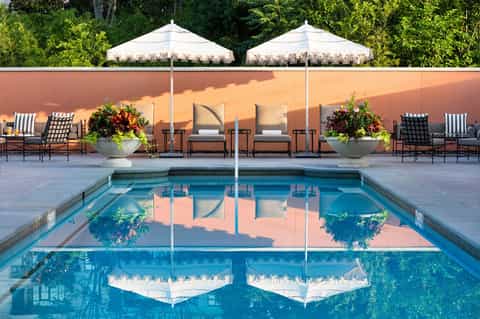 Luxury resort pool with cream umbrellas, white loungers, and terracotta wall backdrop