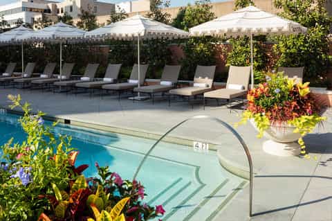 Resort pool with white umbrellas, lounge chairs, and colorful flower planters beside blue water