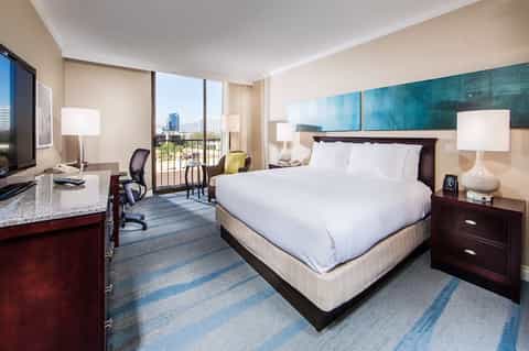 Upscale hotel room with king bed, work desk, and balcony overlooking cityscape