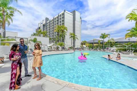 Family enjoying resort pool with modern high-rise hotel building and palm trees in background