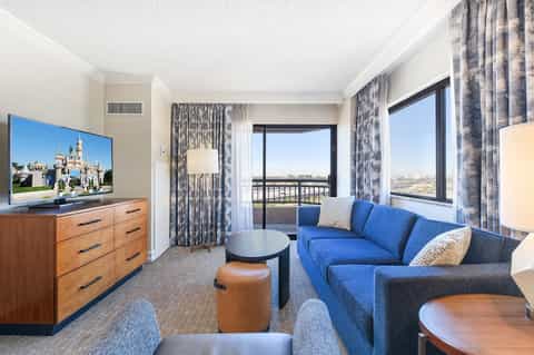 Modern hotel suite with blue sofa, wooden dresser, and panoramic city views