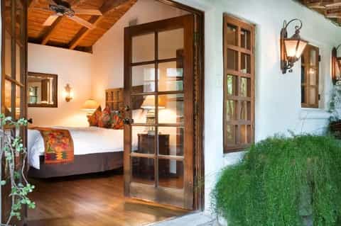 Rustic bedroom with wooden beams, white bedding, and glass doors opening to lush grounds