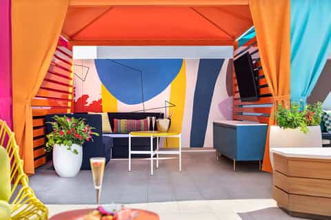 Colorful lounge area with orange fabric canopy, vibrant murals, and contemporary furniture with plants