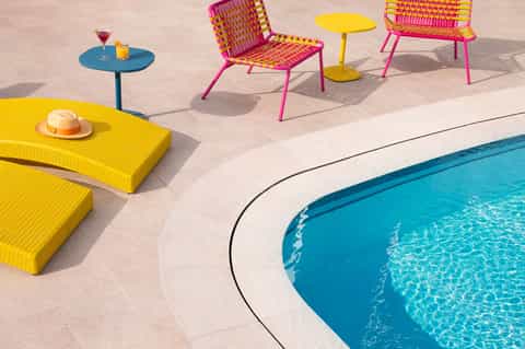 Colorful poolside seating with bright pink and yellow chairs, matching table, and turquoise pool water