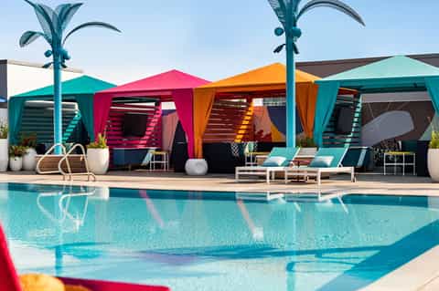 Modern pool area with colorful cabanas in pink, orange, and teal, featuring decorative palm sculptures