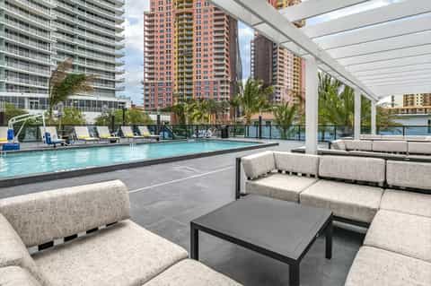 Rooftop pool deck with lounge seating, white pergola, and cityscape views of tall buildings
