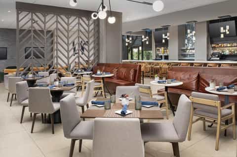 Modern restaurant dining area with geometric wood dividers, brown leather booths, gray upholstered chairs, and pendant lighting