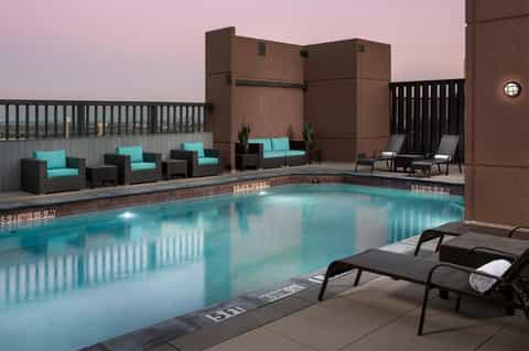 Rooftop pool at dusk with turquoise lounge chairs, seating areas, and brick building backdrop