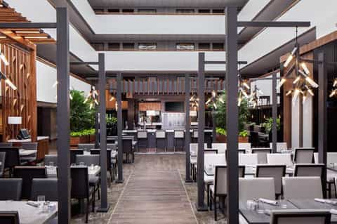 Contemporary outdoor dining area with dark structural beams, wooden accents, and multiple dining tables under covered pavilion