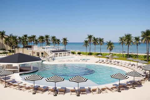 Resort pool with striped umbrellas, lounge chairs, beach and palm trees