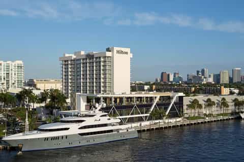 Hilton hotel with luxury yacht docked at riverfront, city skyline in background