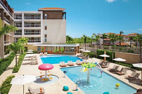 Resort courtyard with two swimming pools, children's play area, lounge chairs, and surrounding multi-story hotel buildings