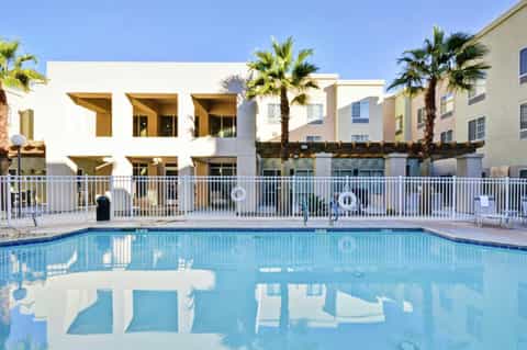 Rectangular swimming pool with white railings in front of modern resort buildings with palm trees