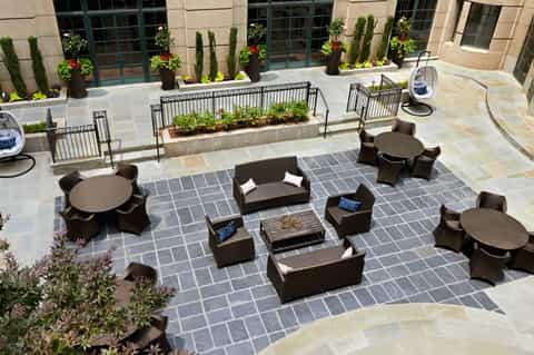 Outdoor courtyard with modern black furniture, round tables, fire pit, planters, and flagstone paving