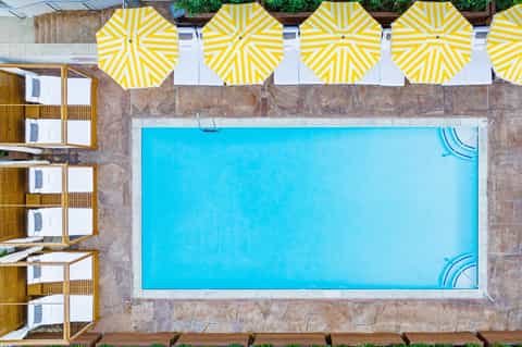 Overhead view of rectangular swimming pool with bright yellow and white striped umbrellas and cabanas