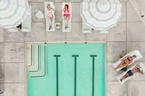 Aerial view of resort pool with guests sunbathing on loungers and under umbrellas