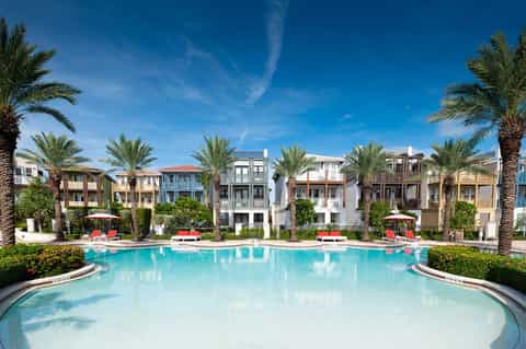 Luxurious resort pool surrounded by palm trees with colorful buildings and red umbrellas