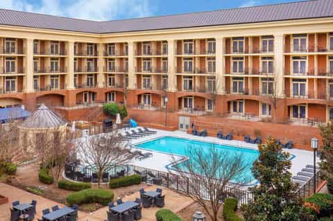 Courtyard view of red brick hotel with multiple stories, balconies, and swimming pool surrounded by lounge chairs