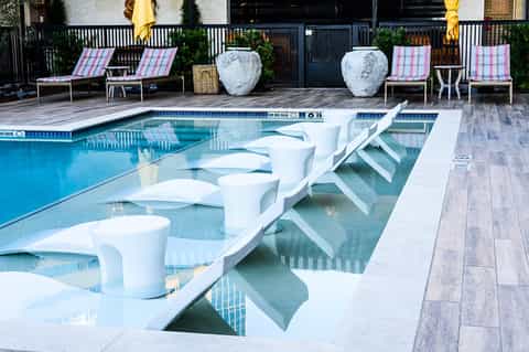 Resort pool with white lounge chairs, pink striped deck chairs, and decorative white planters