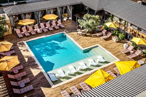 Aerial view of resort pool deck with striped umbrellas, lounge chairs, wooden decking, and striped cabanas