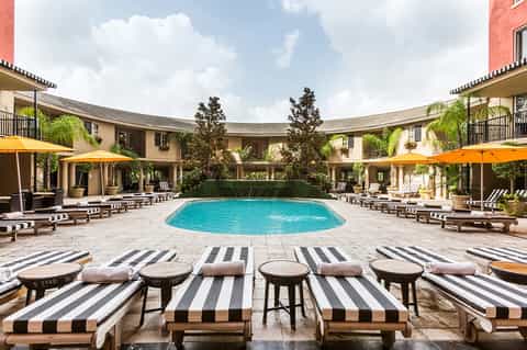 Luxury courtyard pool surrounded by striped lounge chairs, yellow umbrellas, and Mediterranean-style buildings