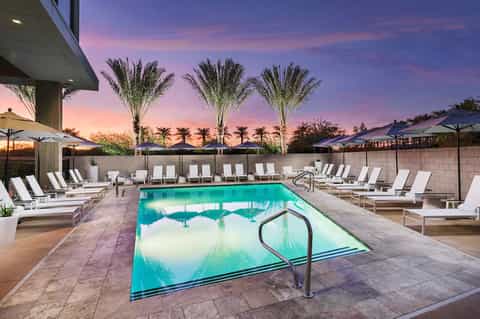 Luxury resort pool at sunset with palm trees, lounge chairs, and umbrellas under purple sky