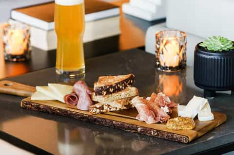 Charcuterie board with cured meats, cheese, bread and beer on black table