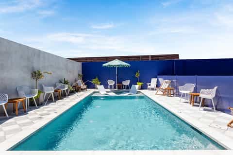 Resort rooftop pool with turquoise water, white loungers, blue umbrellas, and contemporary outdoor seating