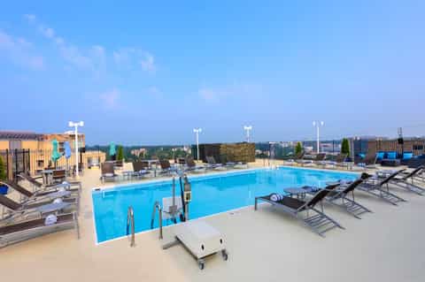 Rooftop pool with blue water, lounge chairs, and city skyline views under clear sky